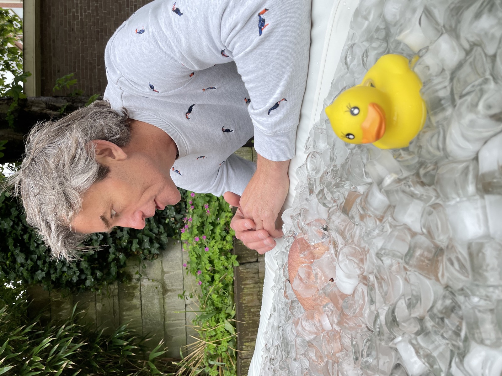 Jeroen leunt over de rand van een ijsbad, met een badeend tussen de ijsblokken.